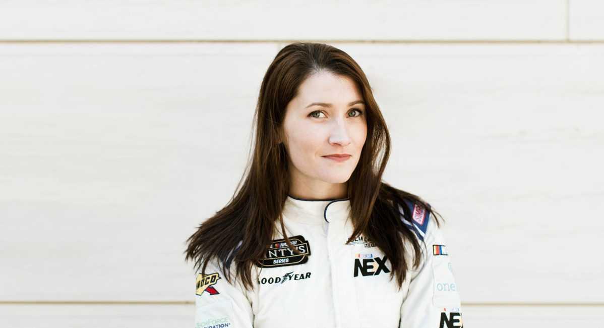 Julia Landauer standing against a white wall in a race suit
